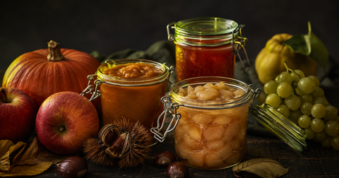 Bocaux de conserves d'automne — compote de pommes, gelée de coing et purée de courge entourés de fruits et légumes de saison.