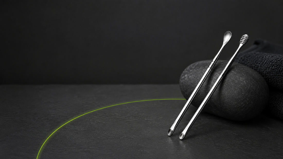 Un set de cure-oreilles oriculi en acier inoxydable poli argenté.posé sur une surface sombre texturée. Fond uni gris anthracite très foncé. Ambiance salle de bain minimaliste et premium, zéro déchet.