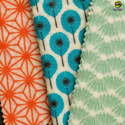 Gros plan sur les 3 motifs de beewrap L'embeillage. Le premier est un motif de traits en étoile orange, le second des fleurs bleus et le dernier des traits verts qui font penser à des feuilles.