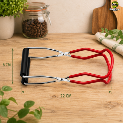 Pince à bocaux en inox rouge, posée à plat sur un plan de travail de cuisine. Les dimensions sont indiquées en cm.