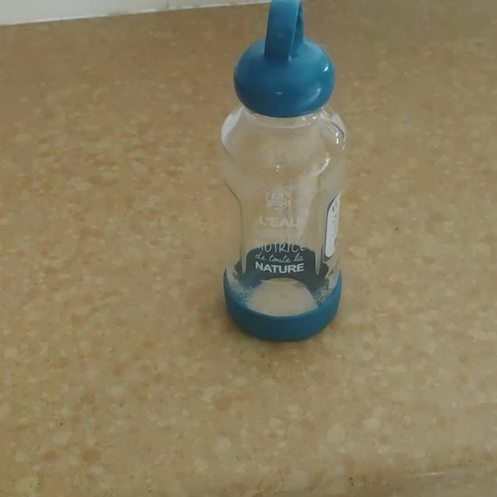 Présentation d’une gourde de 500 ml en verre borosilicate avec bouchon d’origine végétale, anneau de transport et base recyclée amovible. La vidéo montre le démontage de la gourde et précise qu’elle est fabriquée et assemblée en France.